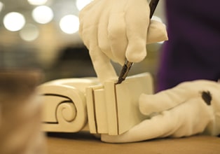 Gloved hands of a KraftMaid finish artisan applying glaze highlights to a corbel