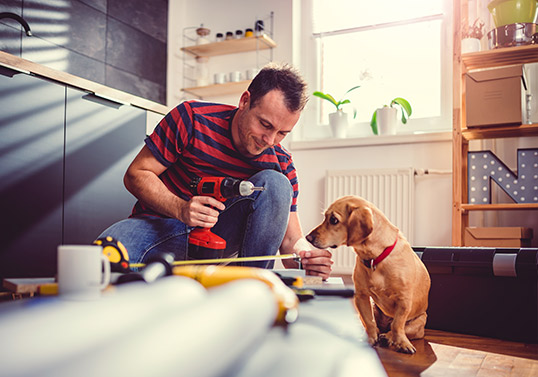 Man with drill and tape measure preparing to finish kitchen cabinet installation